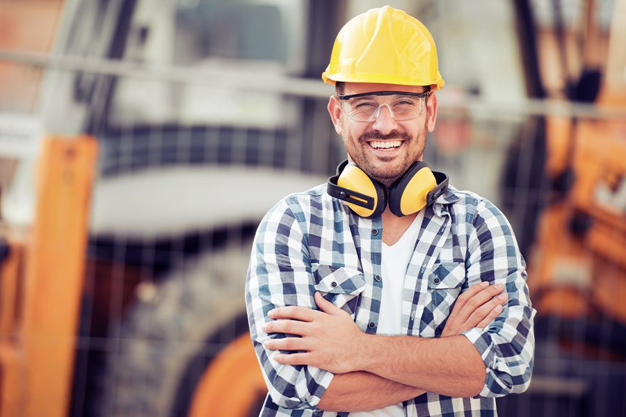 Specialized Business Insurance - Construction Worker in Hard Hat Smiling at Camera in Front of Construction Equipment